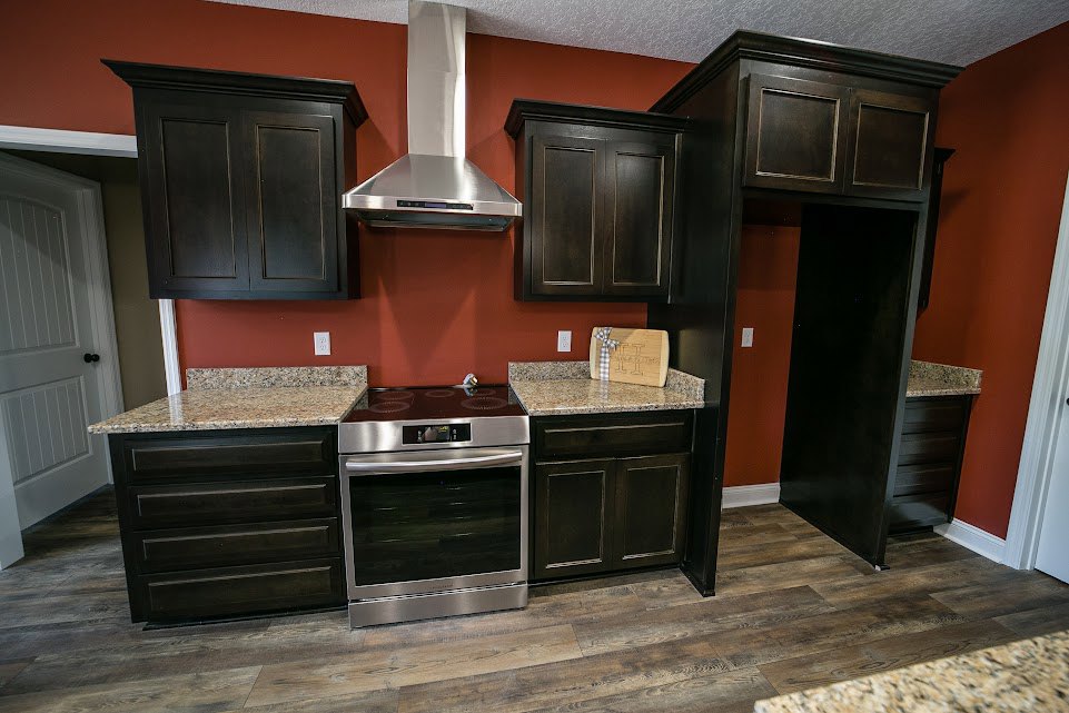 Black kitchen cabinets with granite countertops, stainless steel oven, white door with black knob, sunlight on white wall, silver kitchen utensil, wooden block with decorative bow