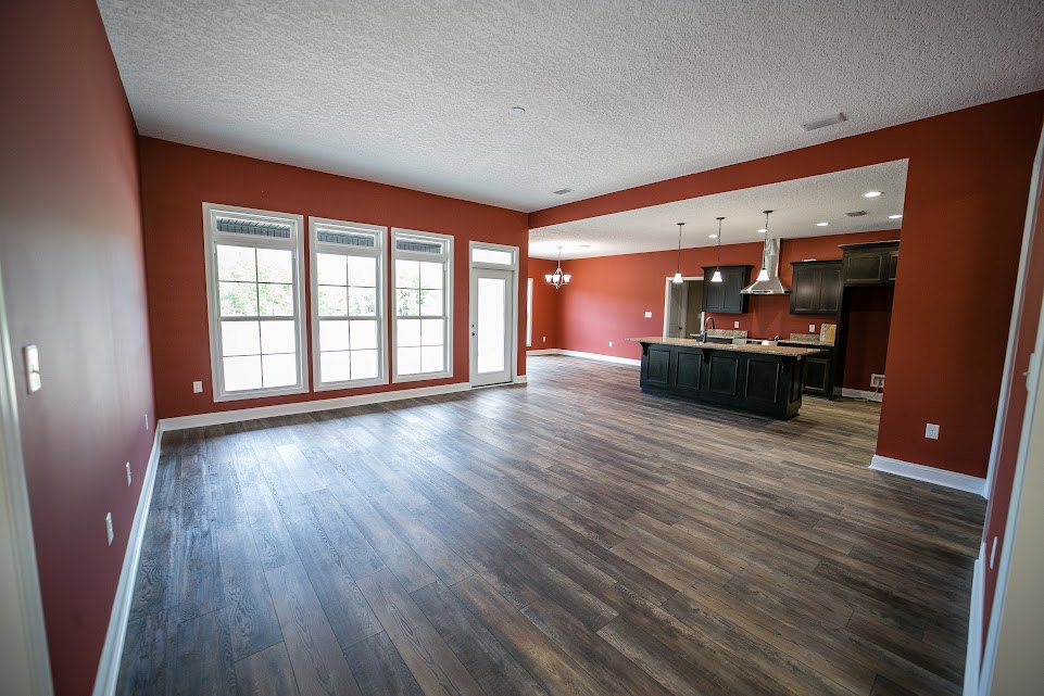 Open-concept living area with hardwood floors, black kitchen island topped with marble, and a row of white-framed windows along one wall