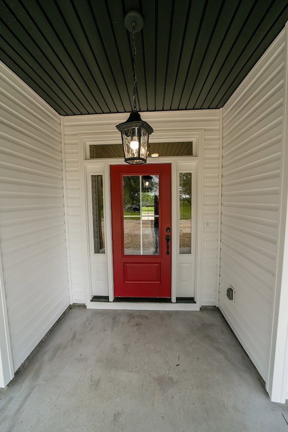 Red door with a rectangular glass pane, white trim, concrete floor, and ceiling-mounted light fixture in a modern entryway.