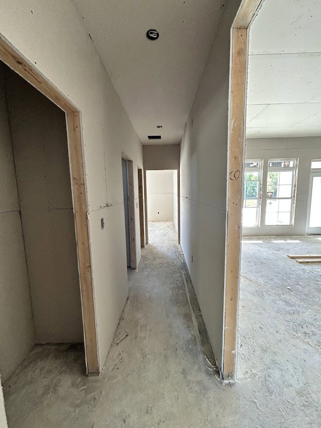Hallway with white paneled door open, leading to room with white walls, multiple windows, and light tile flooring