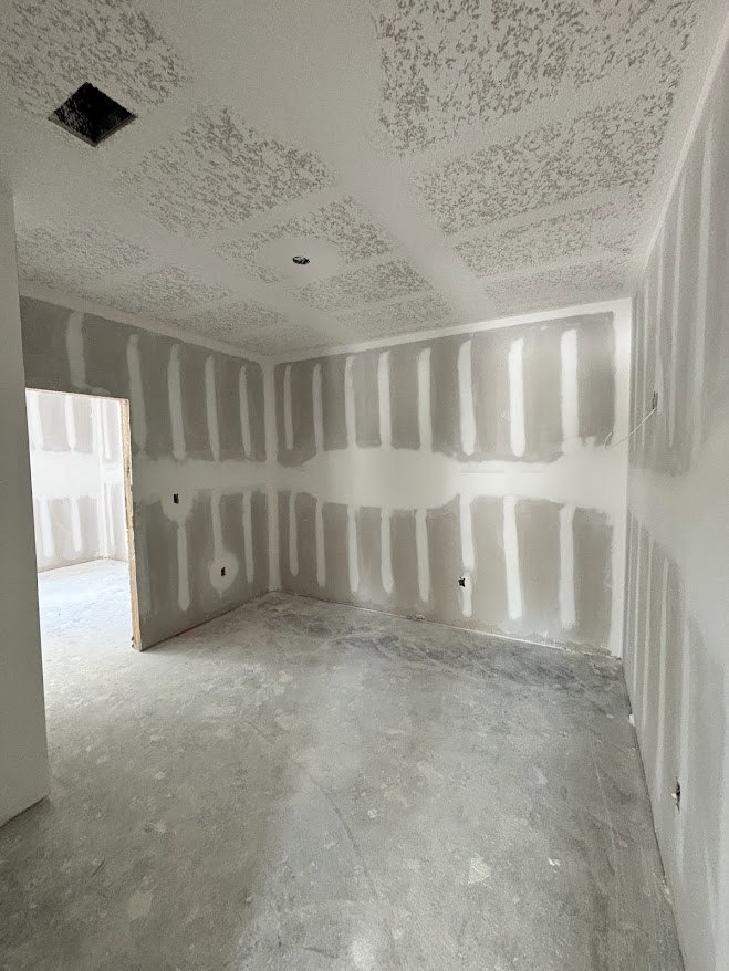 White-walled room with smooth plaster finish, light-colored floor, ceiling featuring recessed area, white door, and sheer white curtain.