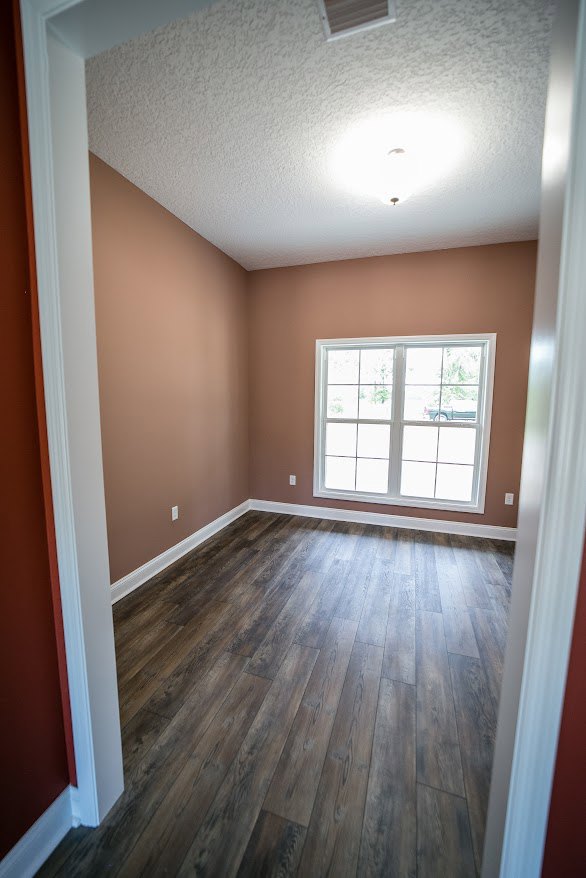 Wood flooring in a bright room with a large white-framed window and smooth plaster walls