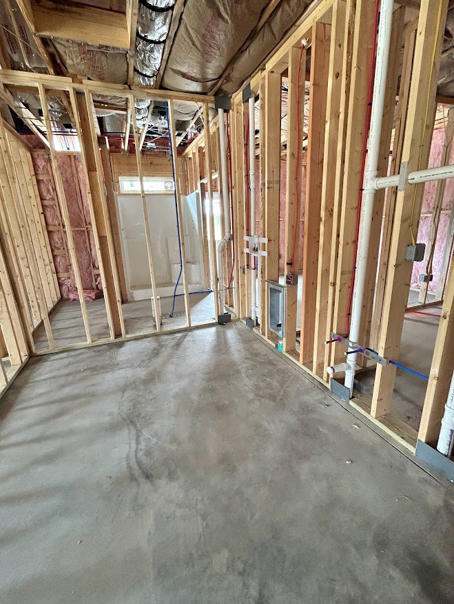 Unfinished room with exposed wood framing, visible plumbing pipes, concrete floor, and partially insulated walls