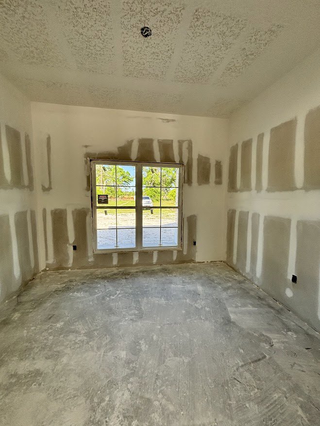 Concrete floor and brown walls in a room with a large window, white stripe detail, plaster ceiling, and circular ceiling fixture.