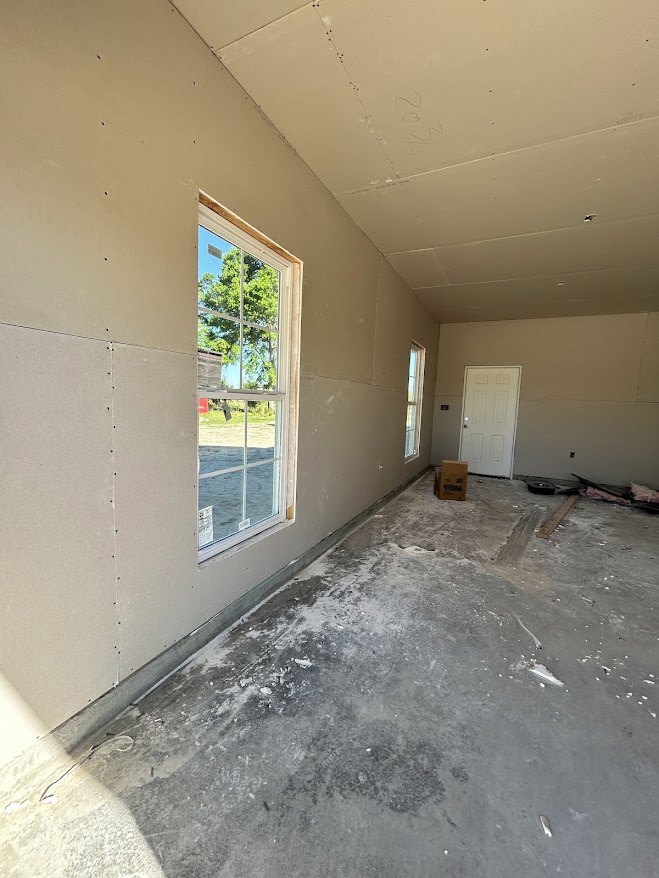 Bright room with smooth white plaster walls, white framed window showing green trees outside, white door with silver handle, light concrete floor, and ceiling.