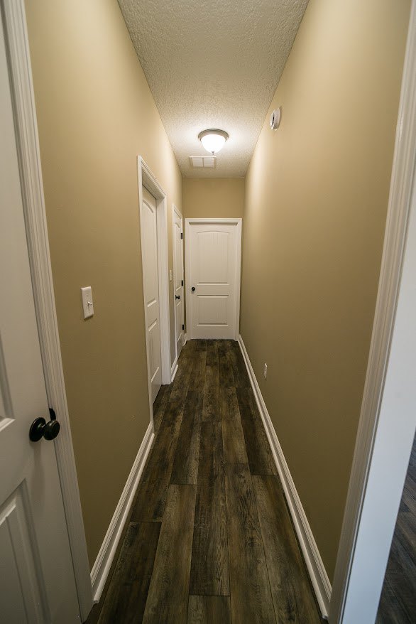 Hallway with white paneled doors, black door knobs, light wood flooring, white plaster walls, and crown molding