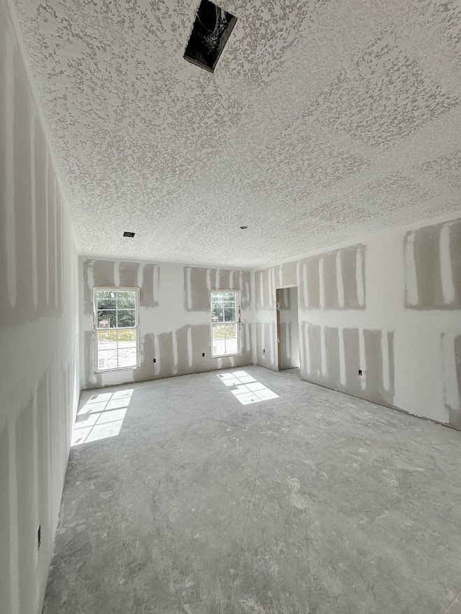 Bright room with smooth white plaster walls, large windows letting in natural light, subtle shadows cast on the white surfaces, and a window displaying an exterior view.
