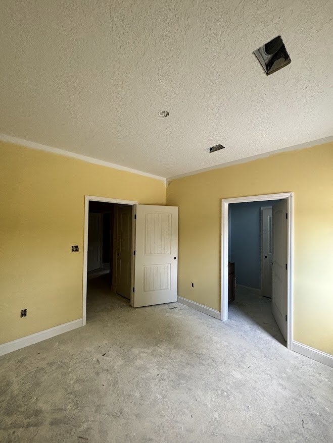 Yellow accent wall contrasts with surrounding white walls, white door with black knobs, black square object on a white surface, hallway lined with white doors, light-colored