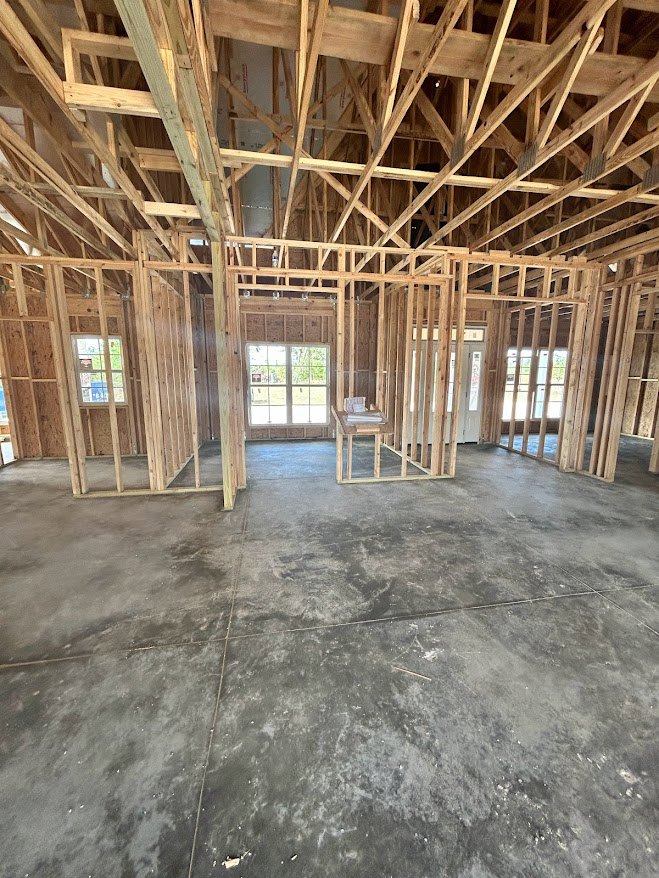 Concrete floor room with exposed wood framing, white-framed window, and table topped with books