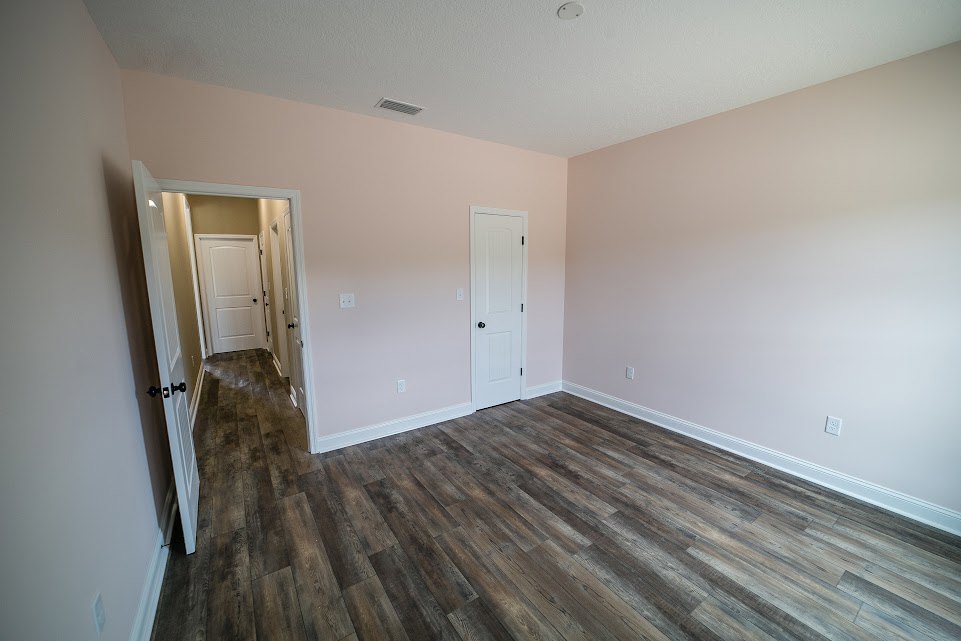 Pink painted walls, light wood flooring, white door with black knob, hallway with additional white doors
