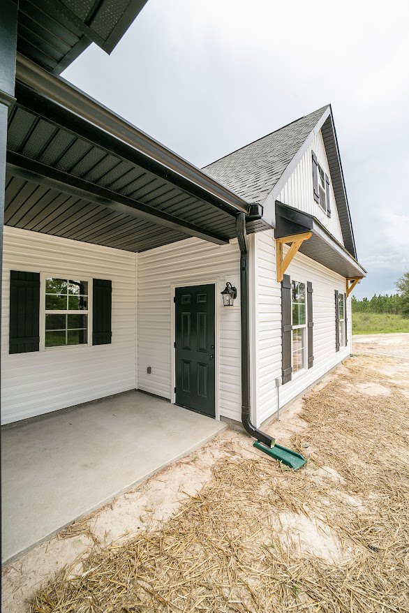 Modern house exterior with black roof, white-framed window, green door, green drain pipe, wooden support beam, and green metal beam lying on grassy ground