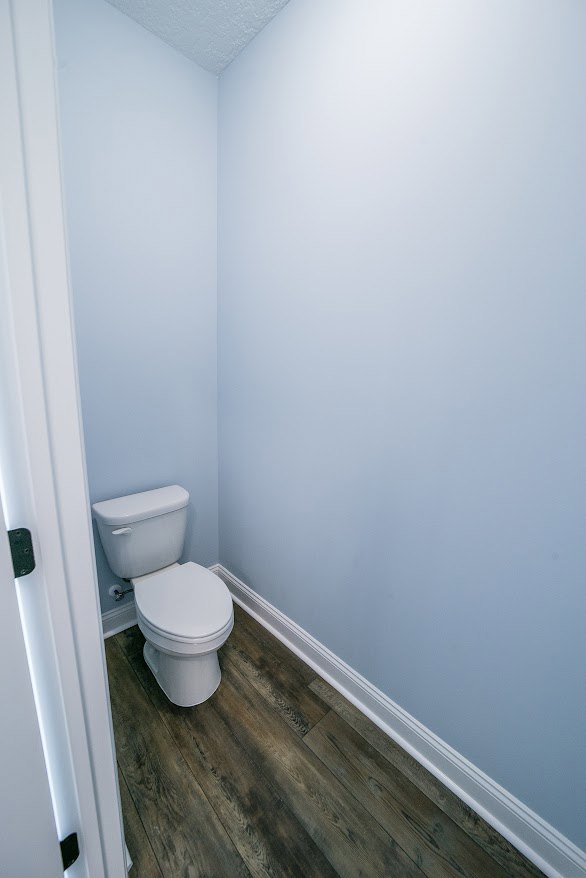 White porcelain toilet with closed lid, mounted against light gray tiled wall, adjacent to chrome flush handle and minimalist bathroom accessories, on smooth tile flooring.