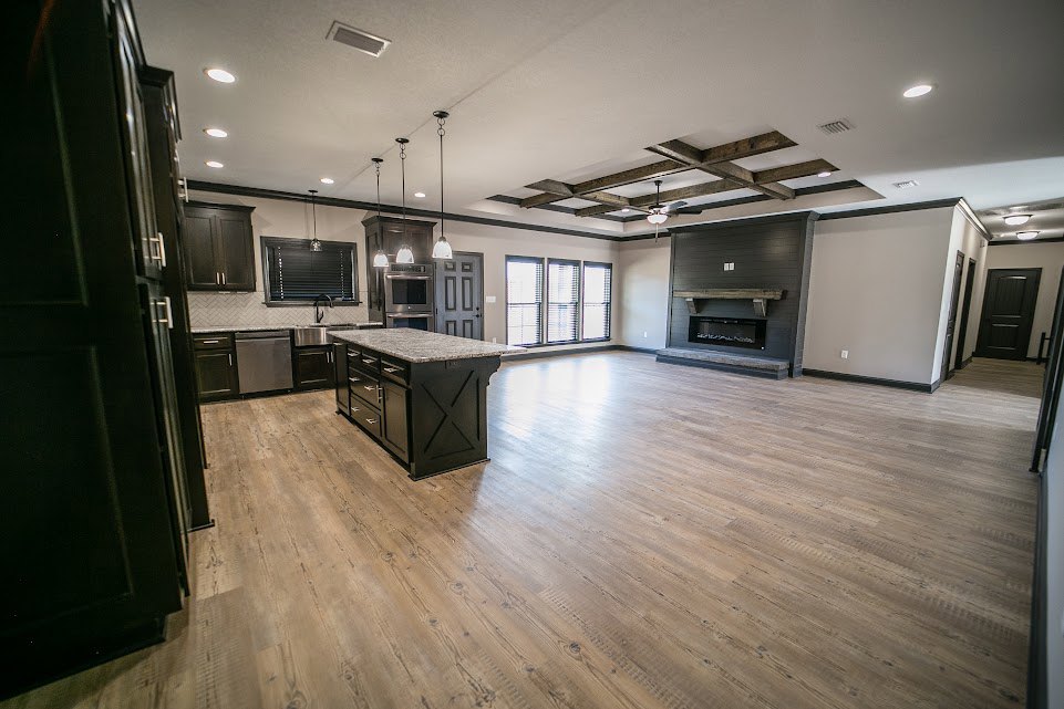 Open-concept kitchen with marble-topped island, wood flooring, white cabinetry, row of windows with blinds, and fireplace along one wall