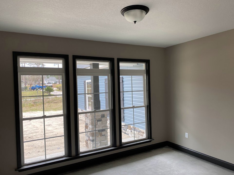 Spacious room with large windows, brick column, ceiling light fixture, white floor with black trim, and view of yard with blue truck