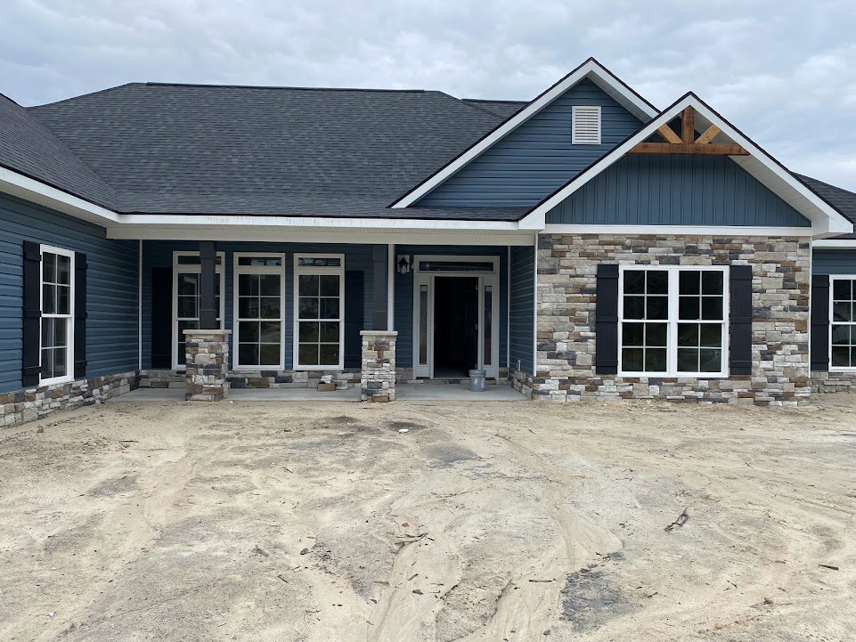 Two-story home with white-framed windows and door, brick porch, dirt driveway, and cloudy sky above