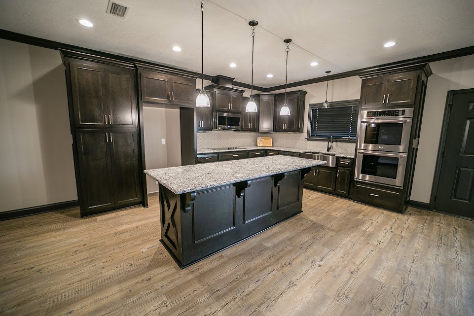 Spacious kitchen featuring a large marble-topped island with a black base, dark wood cabinets with metal handles, built-in microwave, window with white blinds, and light-colored