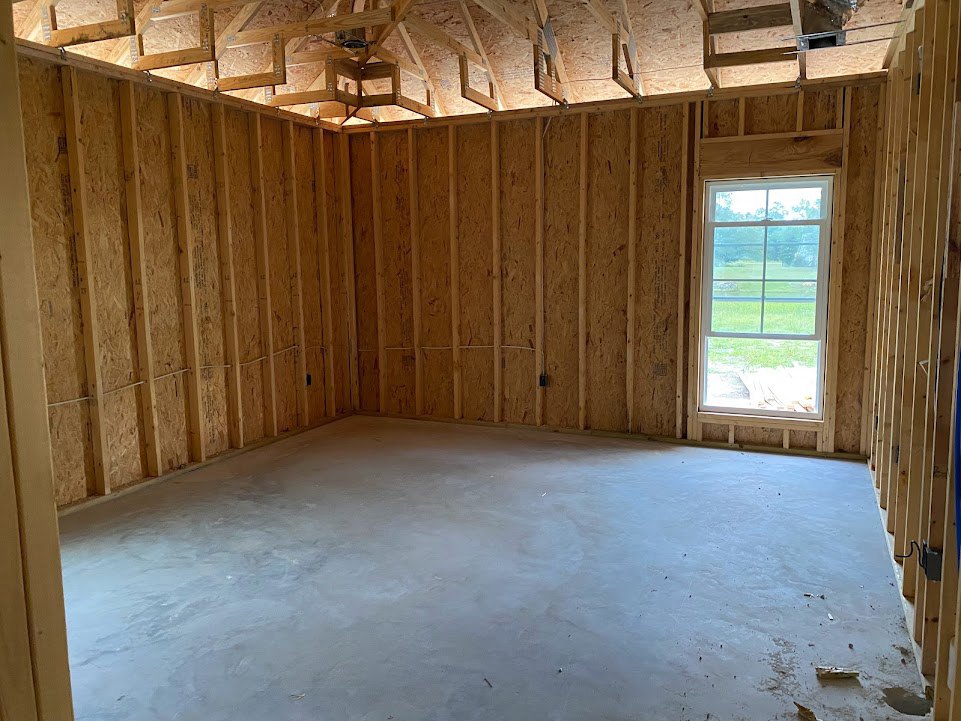 Room with exposed wooden beams and slat accent wall, concrete floor, large window overlooking grassy field