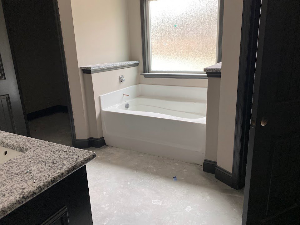 White freestanding bathtub beside frosted glass window, granite countertop with undermount sink, light fixture, and neutral tile walls in modern bathroom