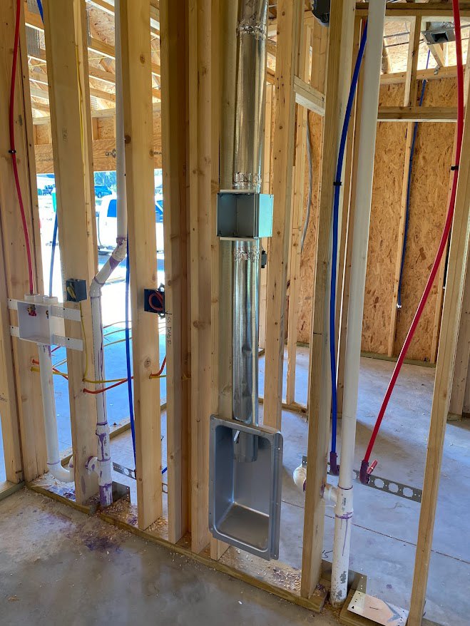 Exposed metal pipe with blue and red hoses running through unfinished wood framing in a residential construction interior