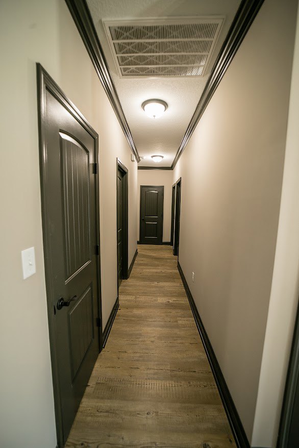 Long hallway with black paneled doors, light wood flooring, white walls, and recessed ceiling lights