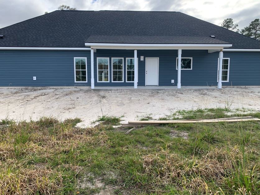 Blue siding house with white pillars on the porch, white framed windows, white front door with black knobs, patchy grass and sandy area in front yard.