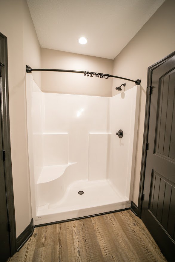 Glass-enclosed shower with chrome fixtures, light gray plaster walls, large-format tile flooring, and white door with modern handle in contemporary bathroom.