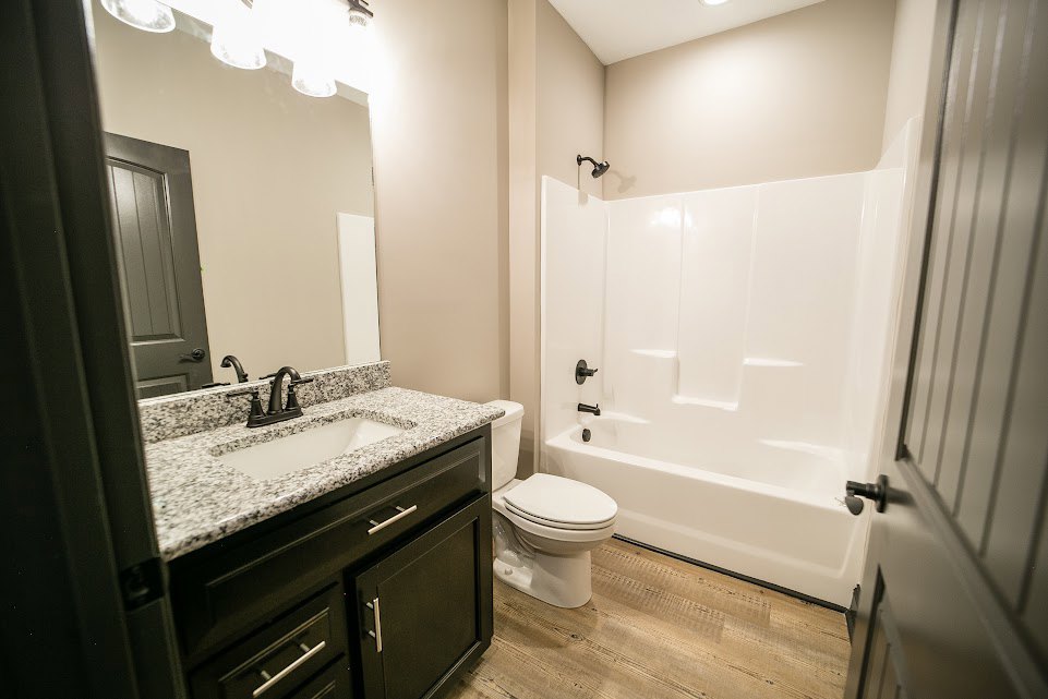 White porcelain sink with chrome faucet set in a stone countertop, adjacent to a modern toilet and freestanding bathtub, surrounded by light tile walls and cabinetry.