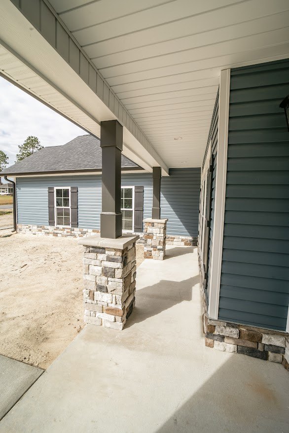 Stone pillars supporting a covered porch, blue horizontal siding, white-trimmed windows, and composite materials on the exterior of a residential home.