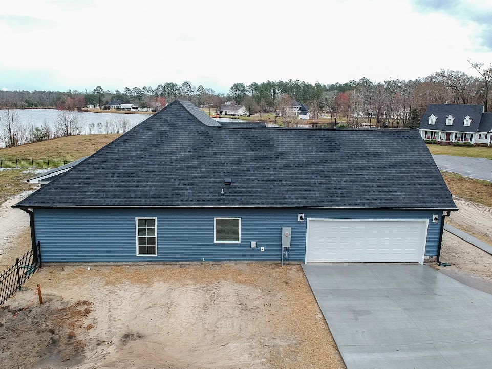 Blue house with white framed square window, white garage door beneath blue roof, concrete driveway bordered by brick wall, tree and cloudy sky in background