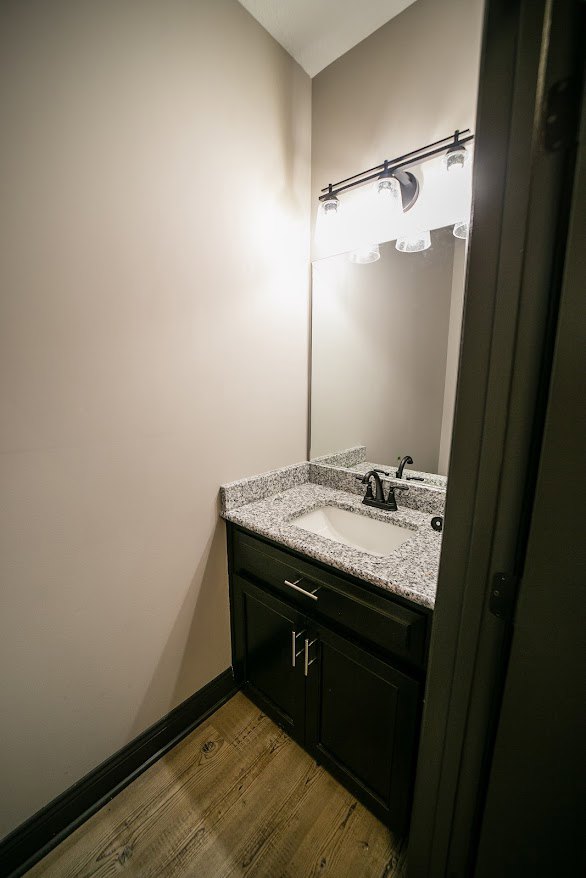 White porcelain sink with chrome faucet set in a light stone countertop, rectangular mirror above, gray tile backsplash, white cabinetry below, and small bathroom accessories on