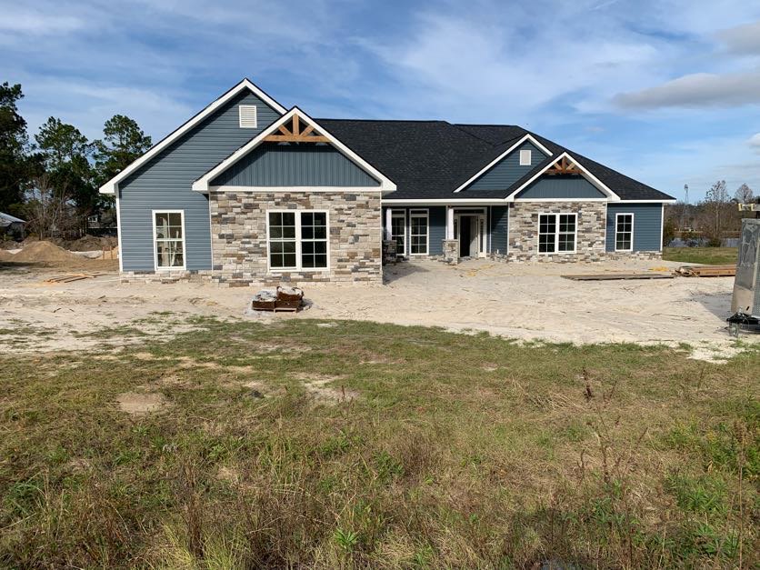 Two-story house with stone and brick exterior, multi-pane windows, expansive green lawn, blue sky overhead, trees in background