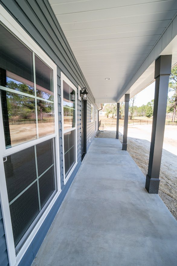 Concrete porch with white ceiling, black and white pillars, single window, lamp fixture, and partial fence