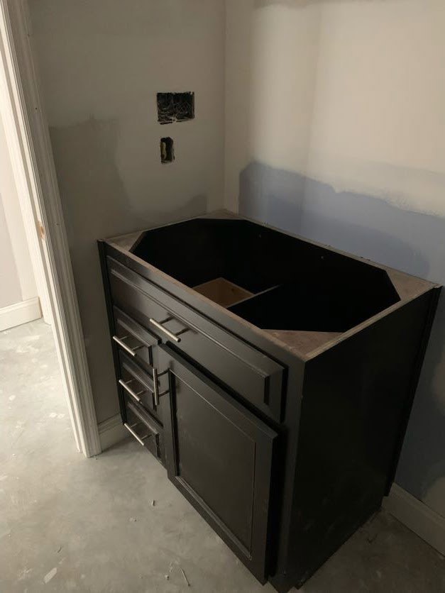 Matte black bathroom vanity with a square cutout in the countertop, white wall backdrop, and grid-patterned drawer fronts.
