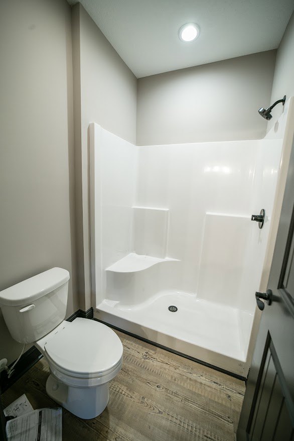 Bathroom with white toilet, glass-enclosed shower, light tile flooring, and neutral wall finishes
