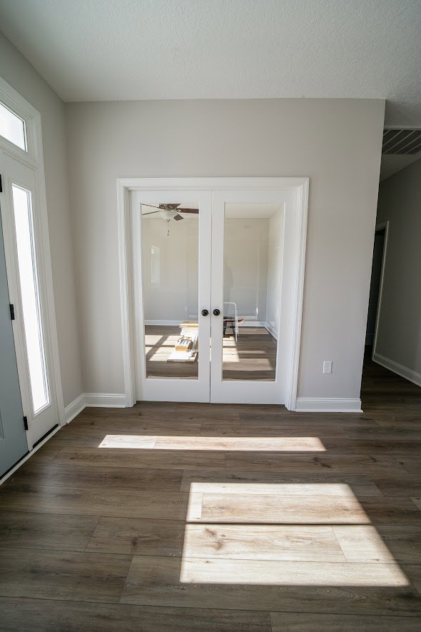 Double glass doors with white trim and molding, sunlight streaming onto wood laminate flooring, plaster walls, and interior design details