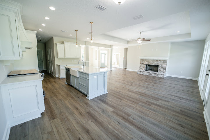 Large open kitchen featuring white cabinets, white countertops, a white sink, fireplace with stone surround, wood and laminate flooring, recessed lighting, and stainless steel