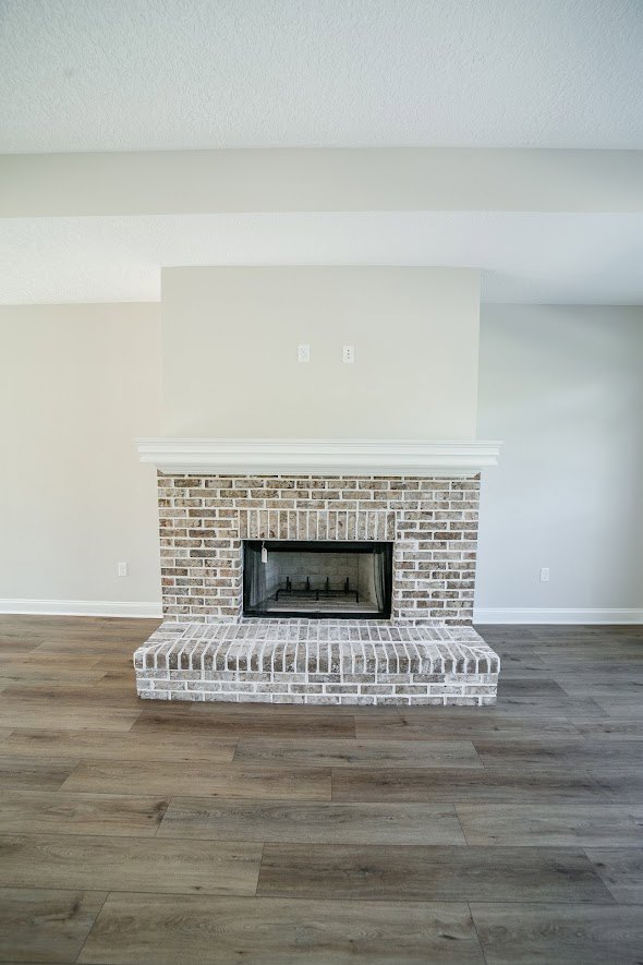 Brick fireplace with black metal frame set against a brick accent wall, wood flooring, and nearby window in a modern living room.