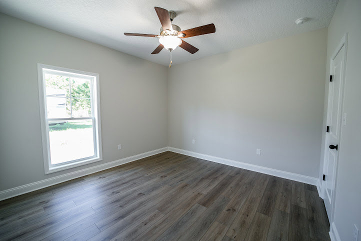 Ceiling fan with light fixture mounted on white plaster ceiling, large window with white trim, wood laminate flooring, neutral walls