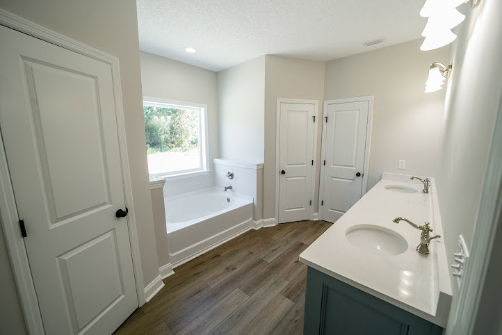 Bathroom with double vanity sinks, chrome faucets, freestanding bathtub, light tile flooring, white cabinetry, and neutral wall tiles