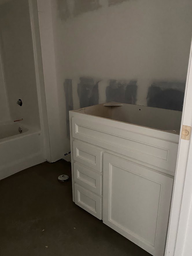 Bathroom with white paneled walls, white cabinet drawers, built-in bathtub featuring a silver faucet, and open white shelving.