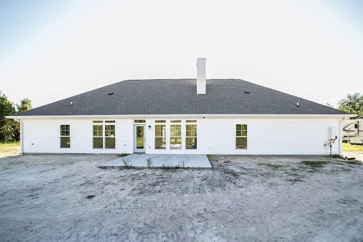White two-story house with black-framed windows, spacious concrete driveway, manicured lawn, and mature trees under a clear blue sky