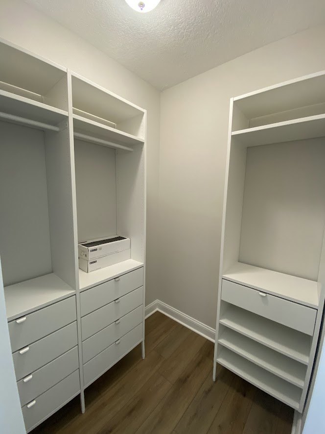 Walk-in closet with white built-in shelves and drawers, wood flooring, and organized storage spaces
