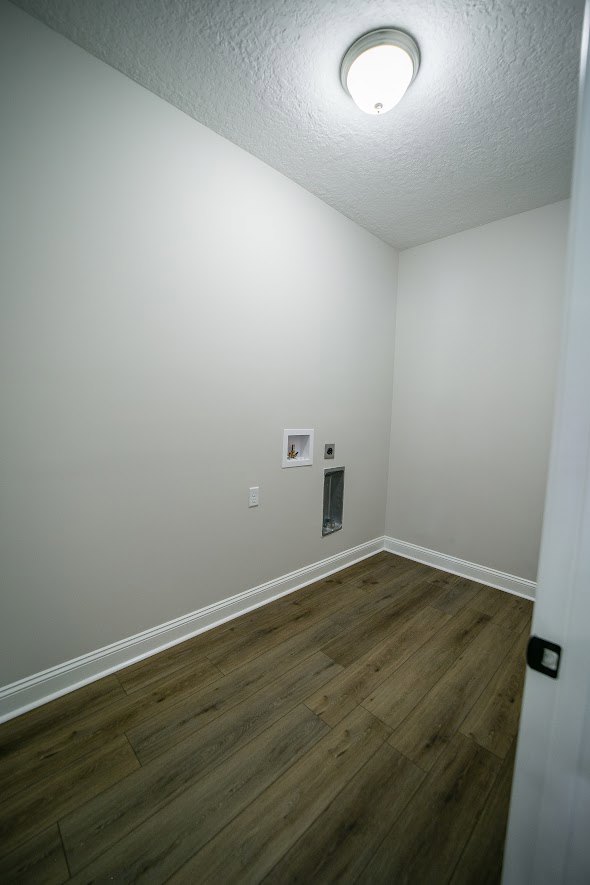 Wood flooring with white baseboards, white plaster wall, ceiling-mounted light fixture