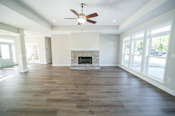 Living room with wood laminate flooring, stone fireplace, ceiling fan, neutral walls, and recessed lighting
