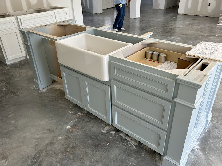 Modern kitchen featuring white cabinetry, stainless steel sink with central drain, light stone countertop, wood flooring, and a person in blue pants standing near the drawers