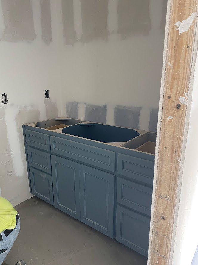 Blue countertop with white wall, stainless steel sink, blue cabinetry, and unfinished hole in wall above sink.