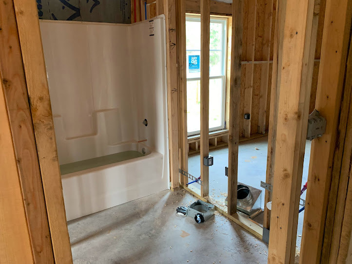 Bathroom featuring a freestanding tub and glass-enclosed shower, surrounded by exposed wood framing, plaster walls, large window, and light-colored flooring.