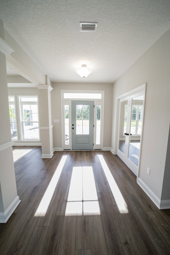 Hallway with wood flooring, white walls, a white door featuring glass panes, and windows allowing natural light