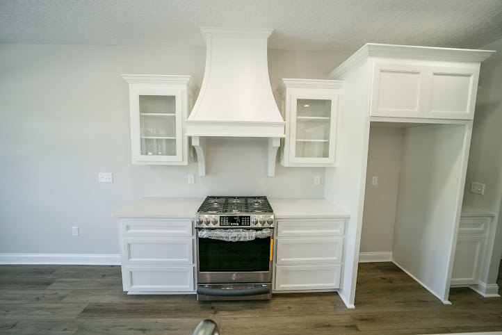 White shaker cabinets with brushed nickel hardware, stainless steel stove, light quartz countertops, and subway tile backsplash in a modern kitchen.