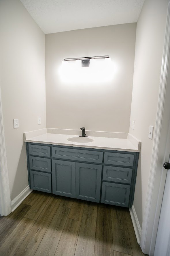 Bathroom with white sink and black faucet, wood flooring, light-colored walls, and modern cabinetry.